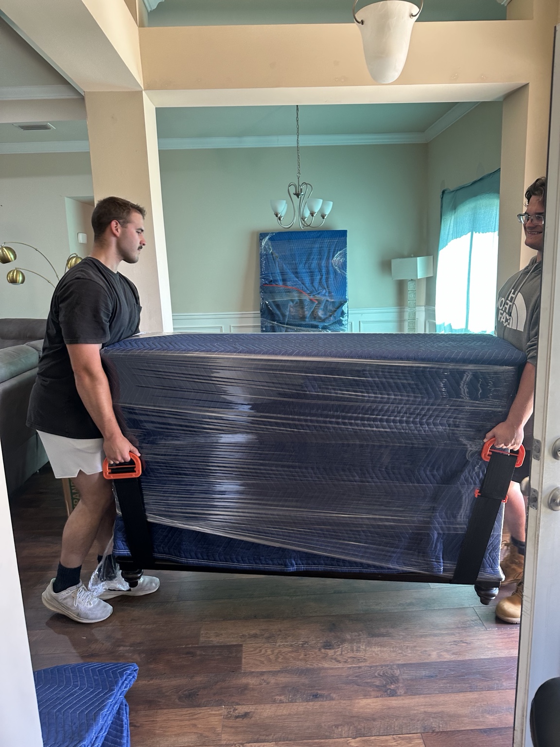 Pure Muscle Moving crew carrying protected furniture inside a customer home