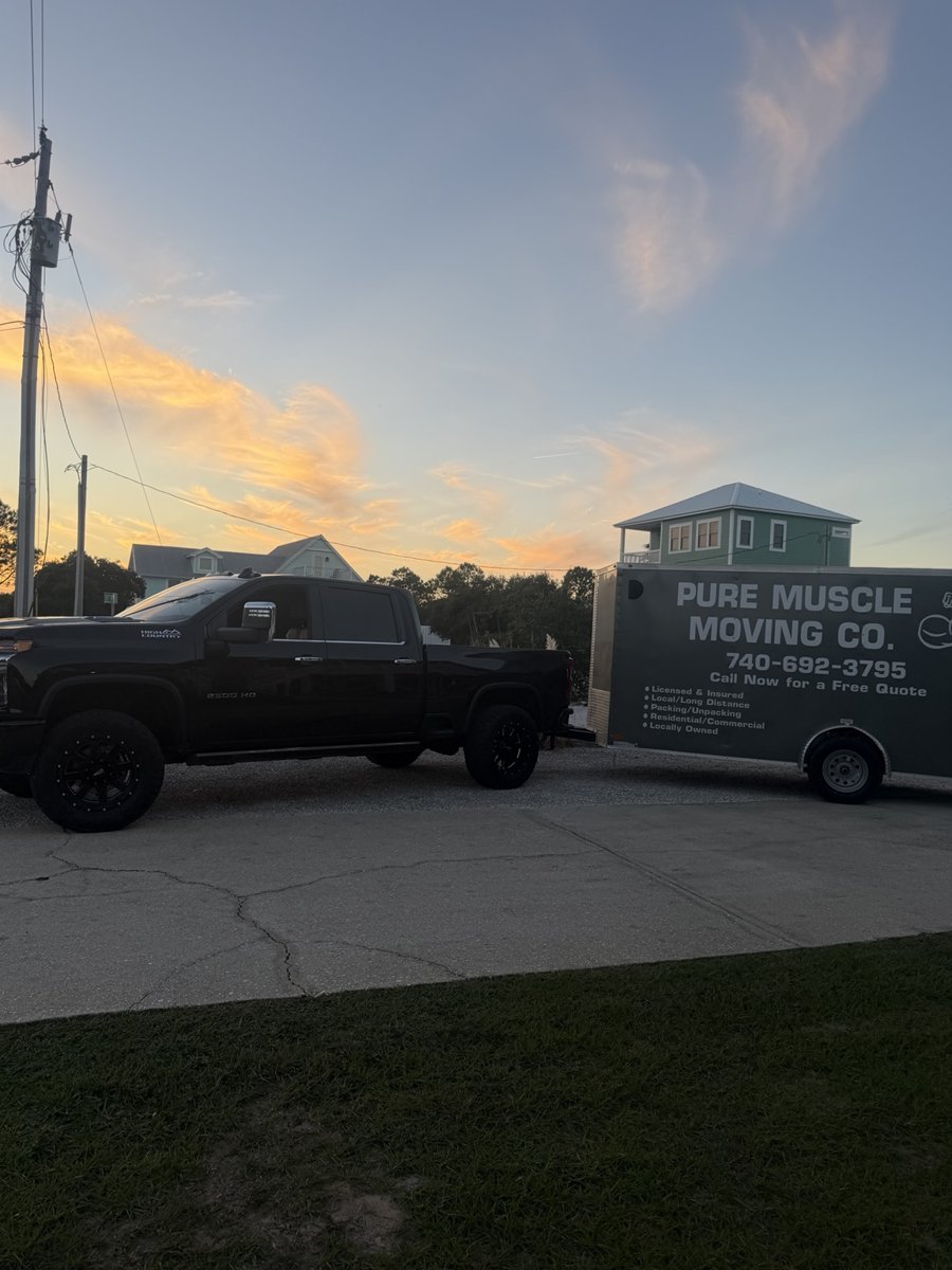 Pure Muscle Moving branded truck and enclosed trailer parked together at sunset